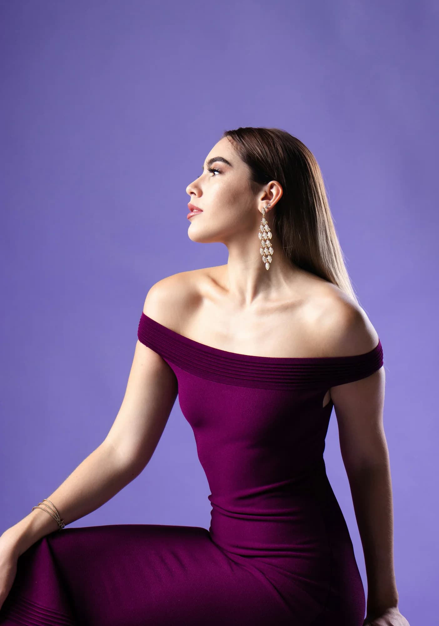 Woman wearing a plum off-the-shoulder top against a violet background