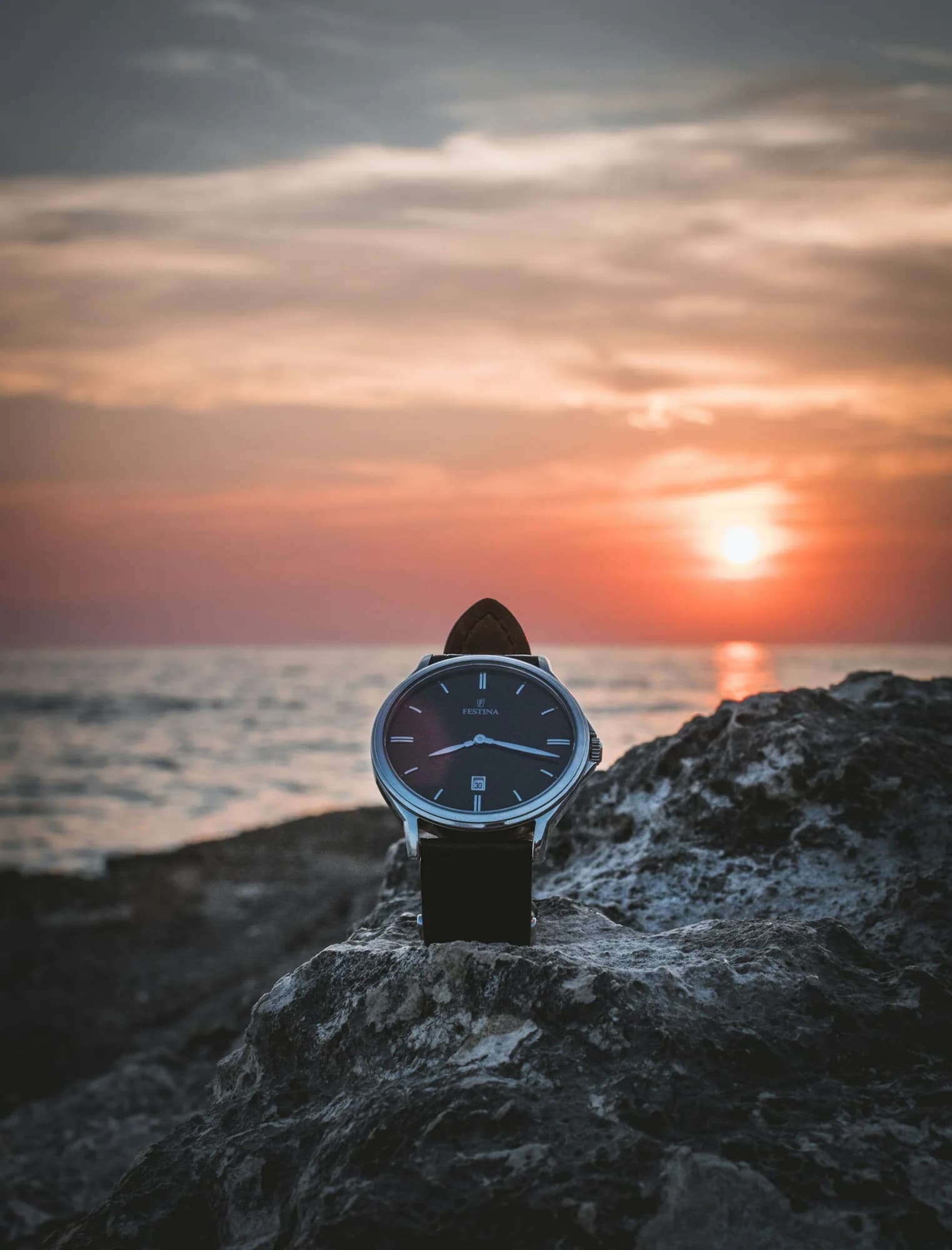 Field watch with a navy dial resting on a rock at sunset