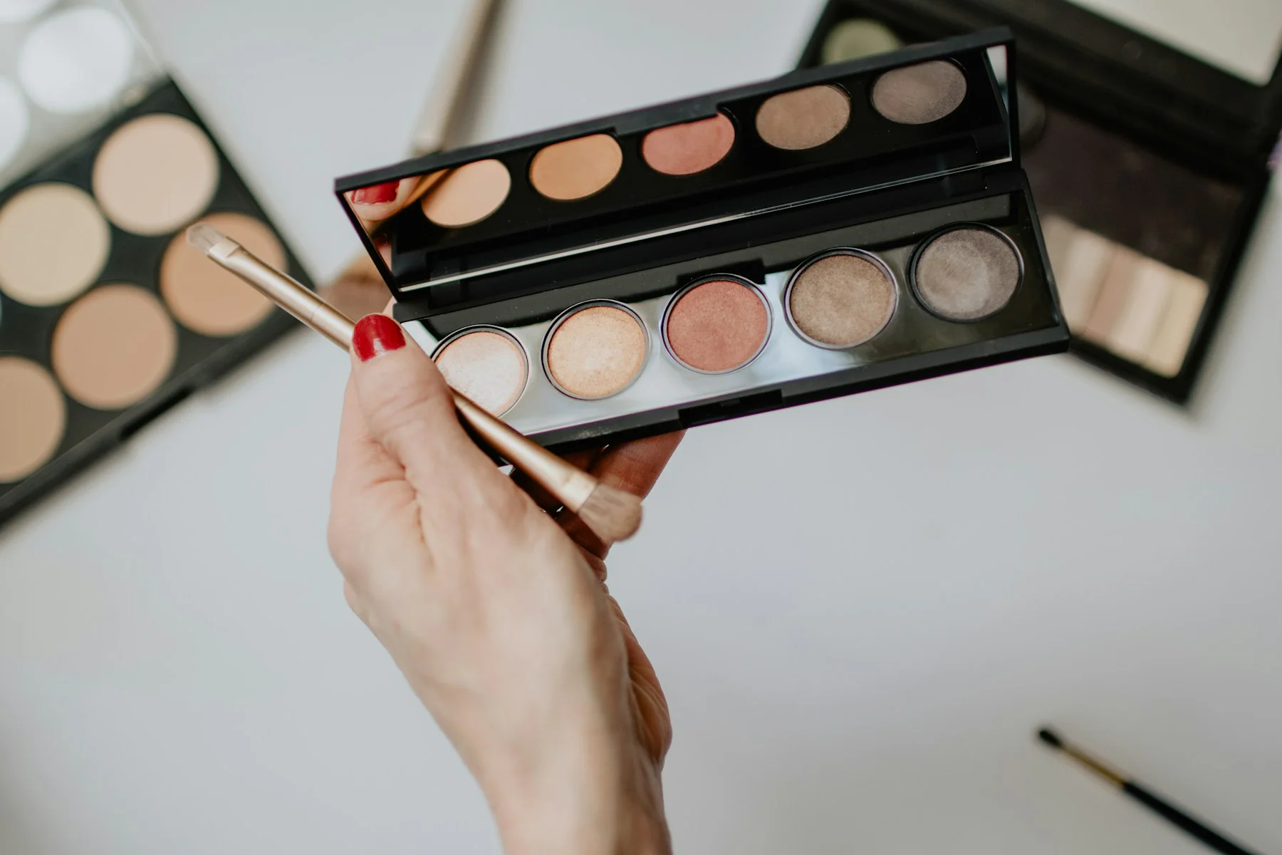 Hand holding a neutral eyeshadow palette with a brush