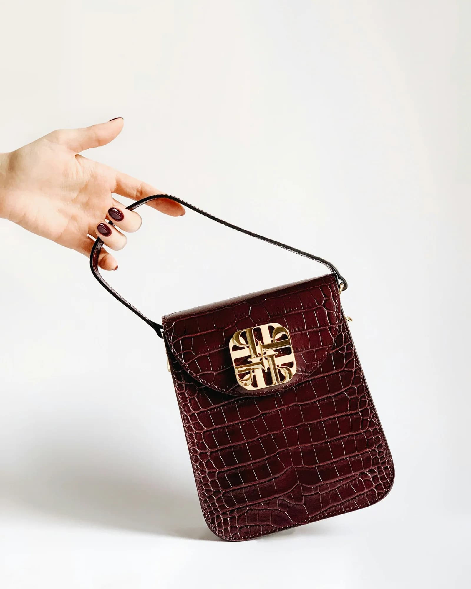 Burgundy croc-embossed mini bag held in hand
