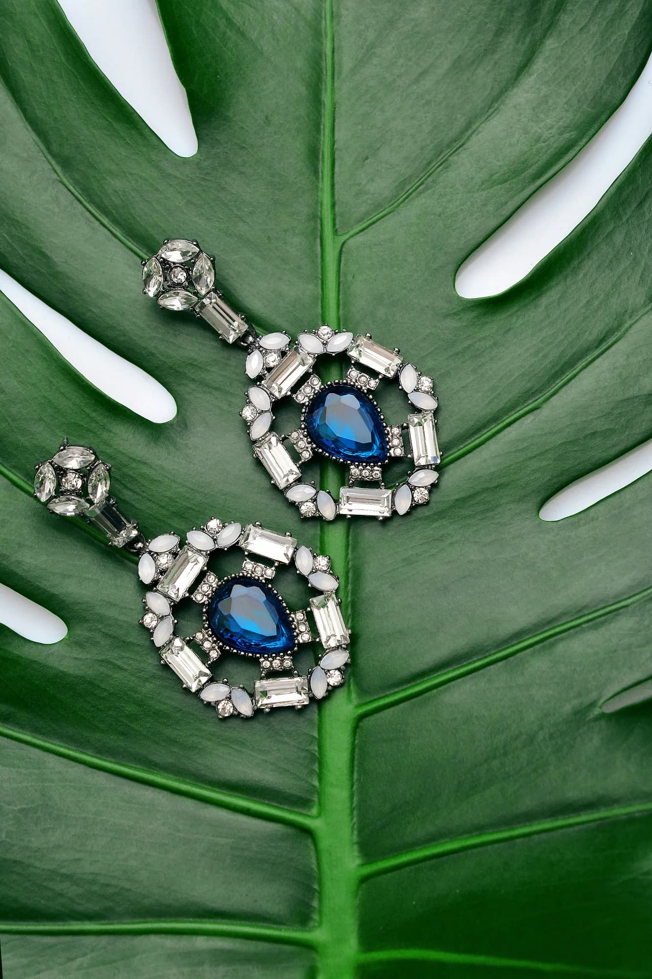 Sapphire drop earrings resting on a green leaf