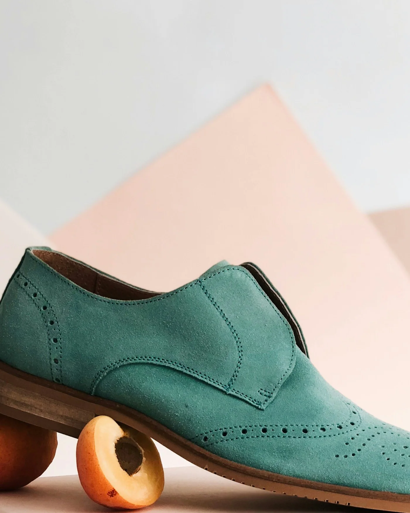 Teal suede loafer displayed on a pink geometric background — detail