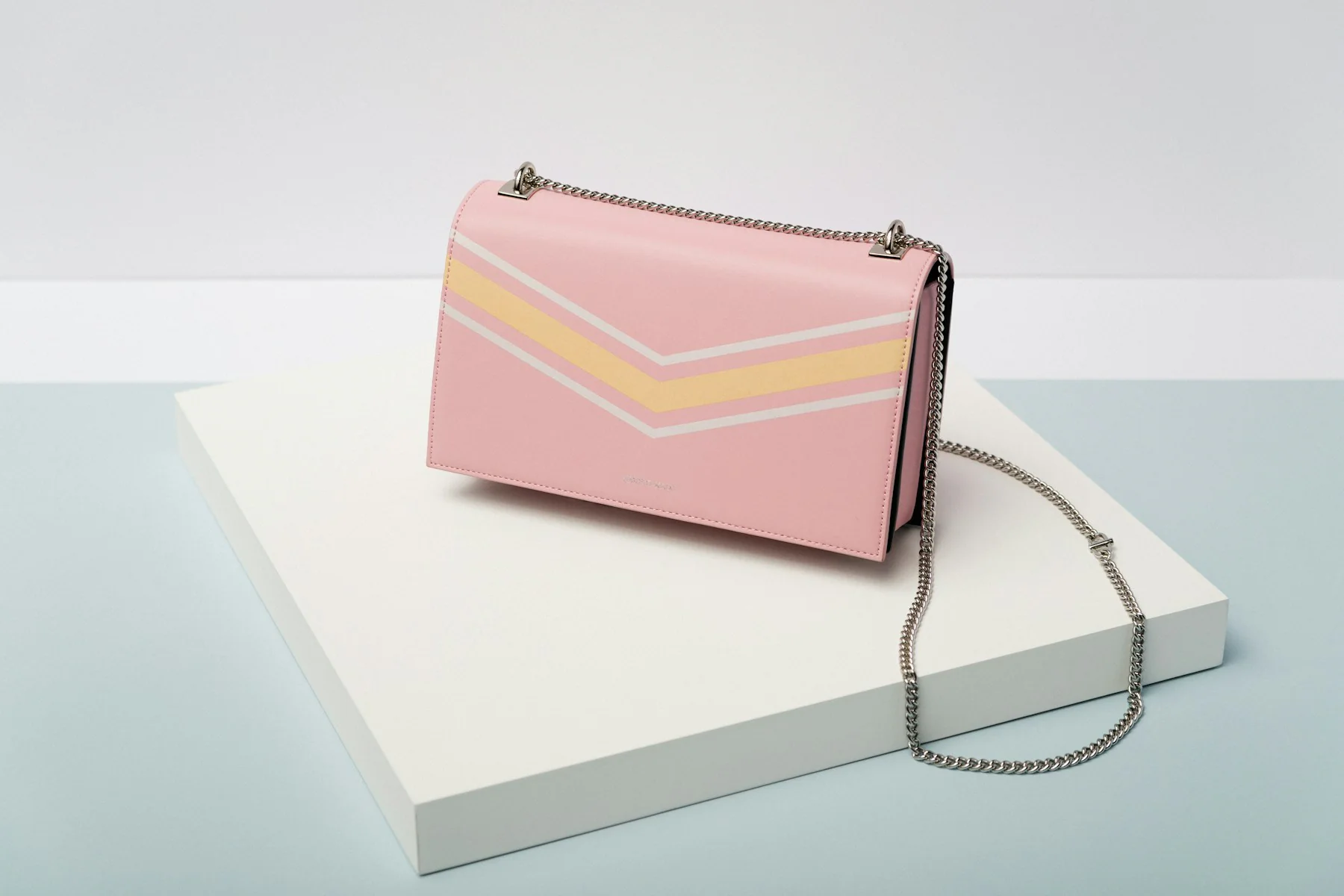 Pink crossbody bag with a chevron flap on a white box