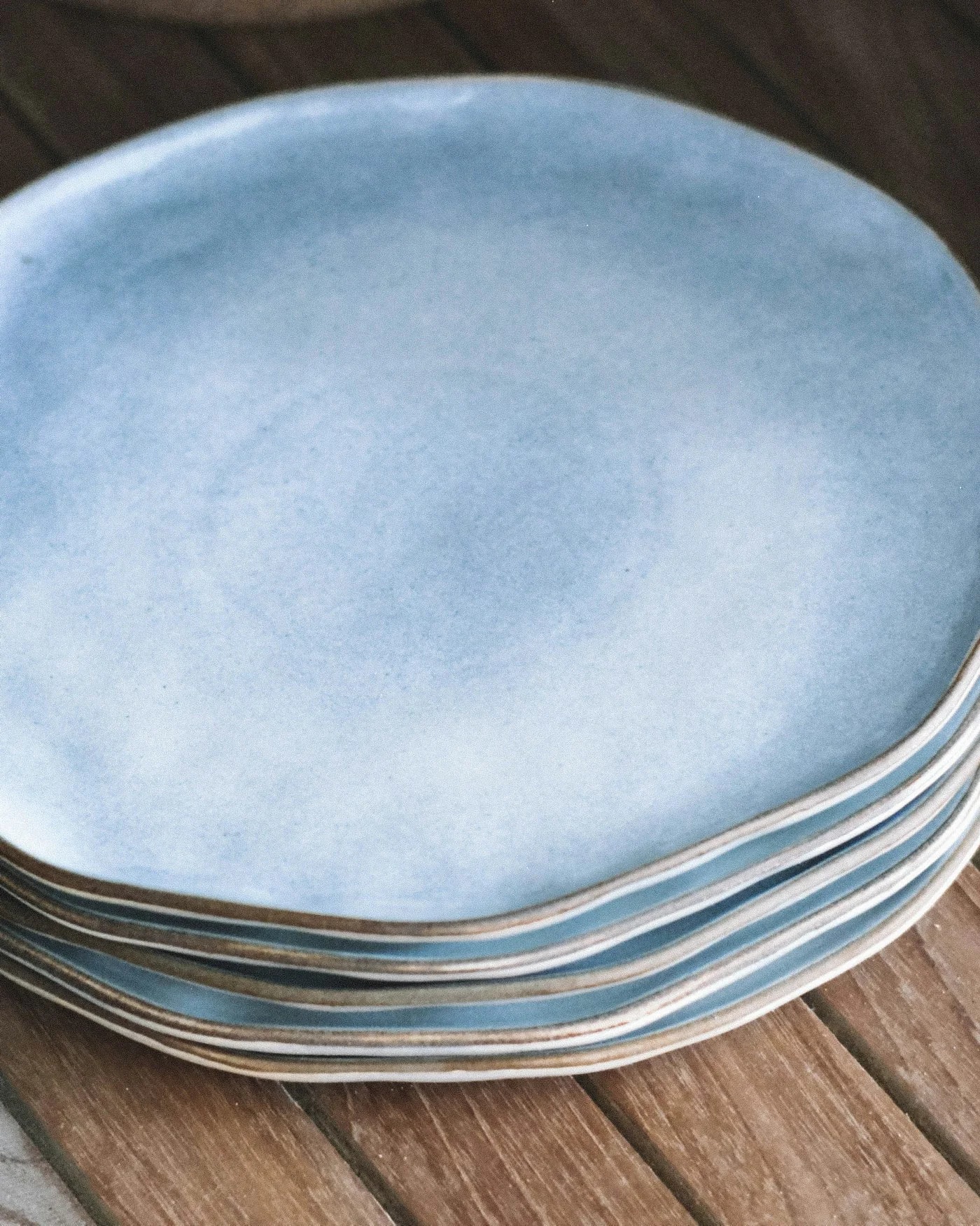 Stack of blue reactive-glaze stoneware plates on a wooden table — detail