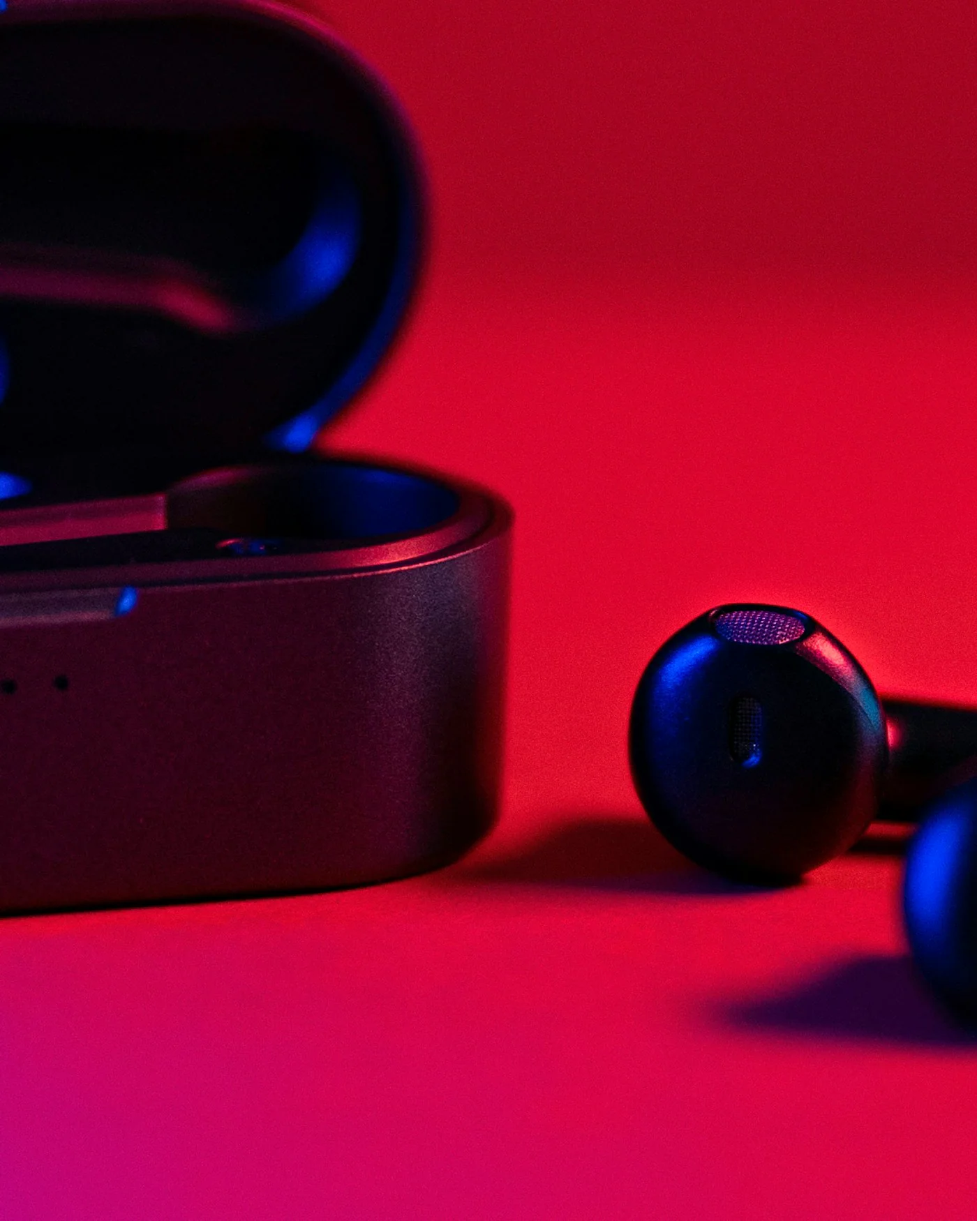 Black wireless earbuds and case on a red background — detail