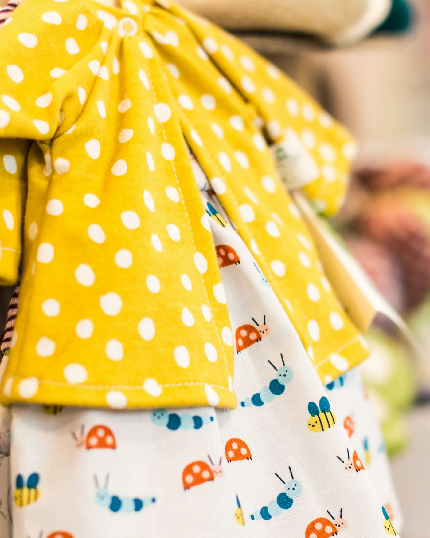 Two children's summer dresses in yellow prints on hangers — detail