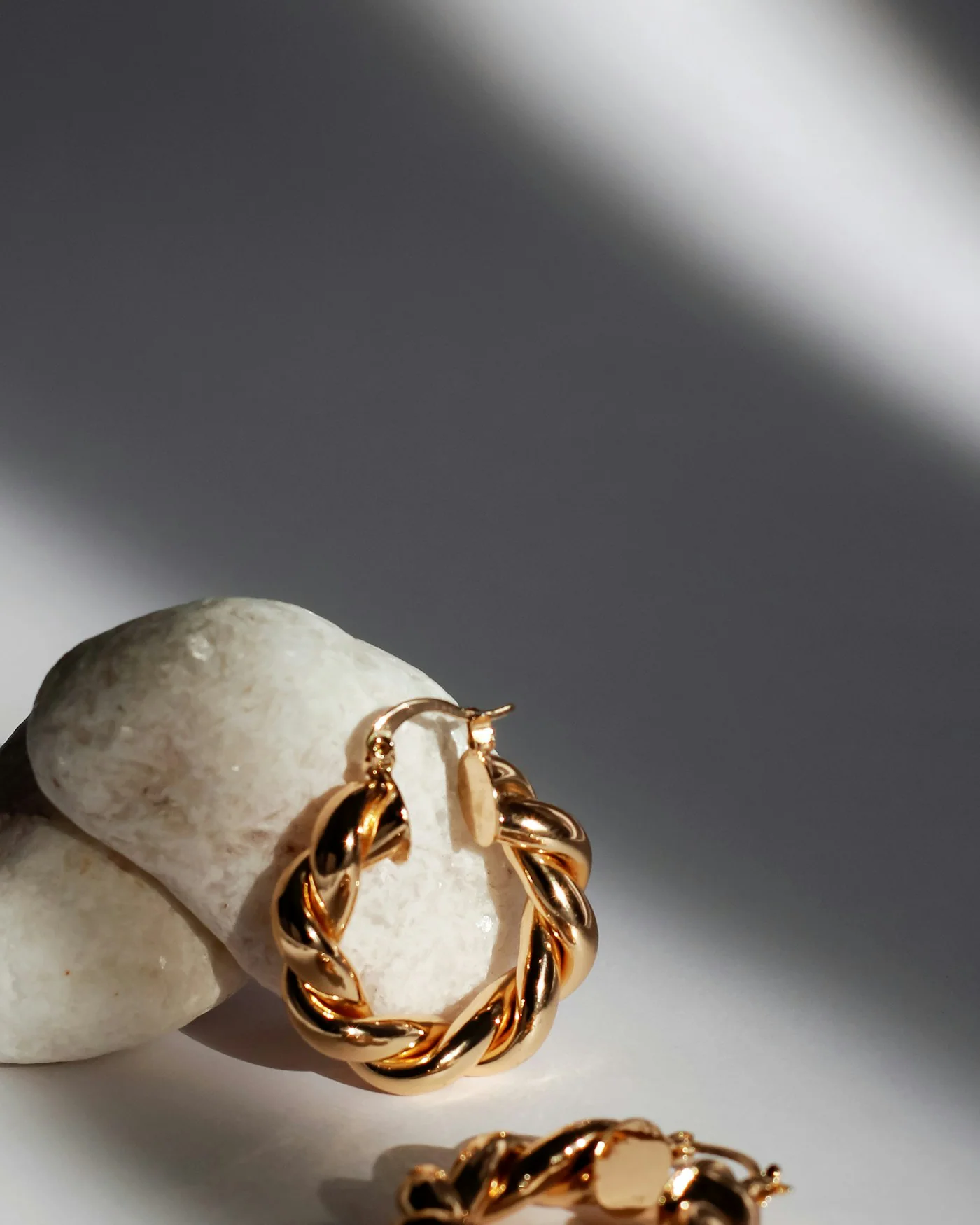Sculpted gold hoop earrings on a white shell — detail