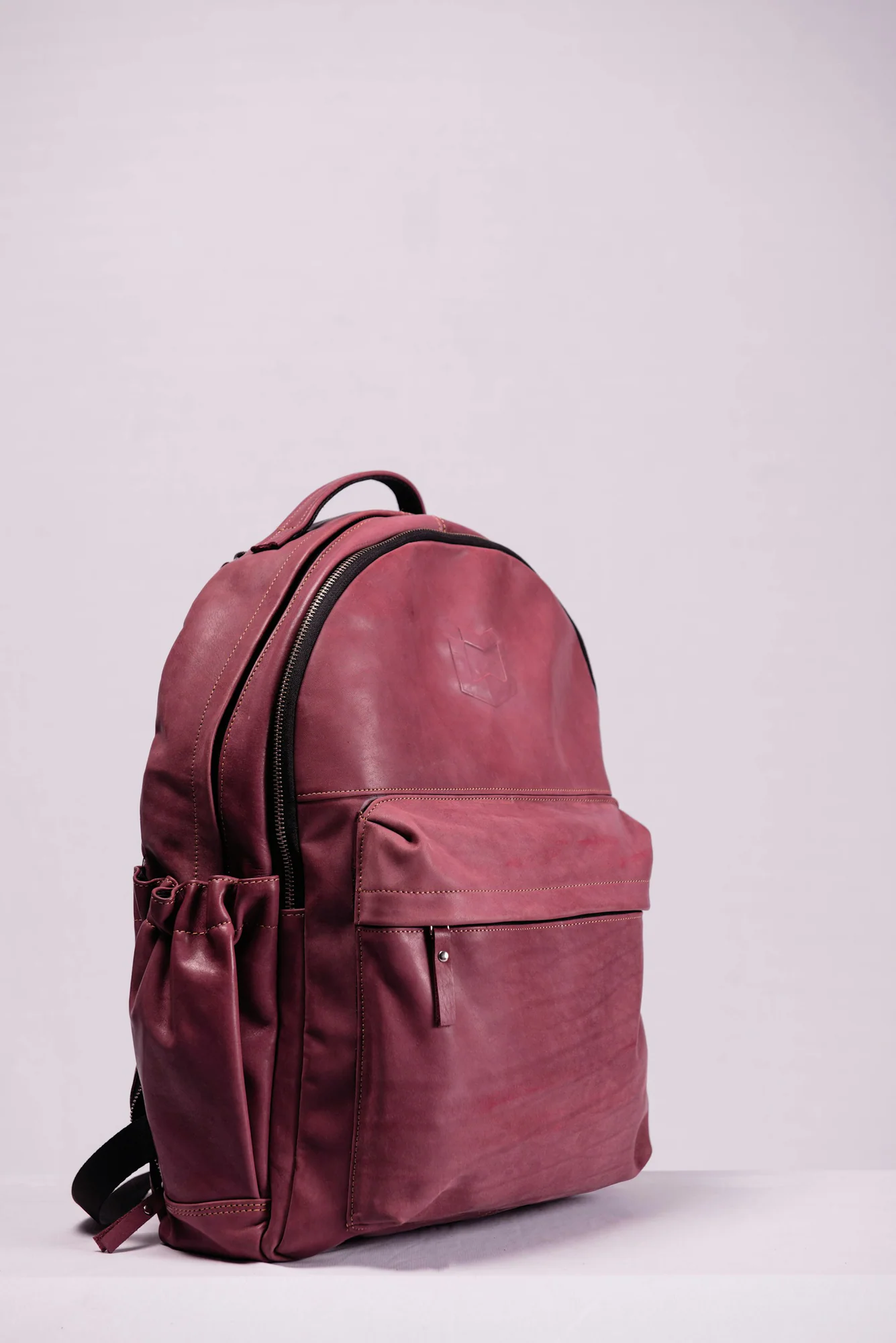 Burgundy leather backpack against a pink background