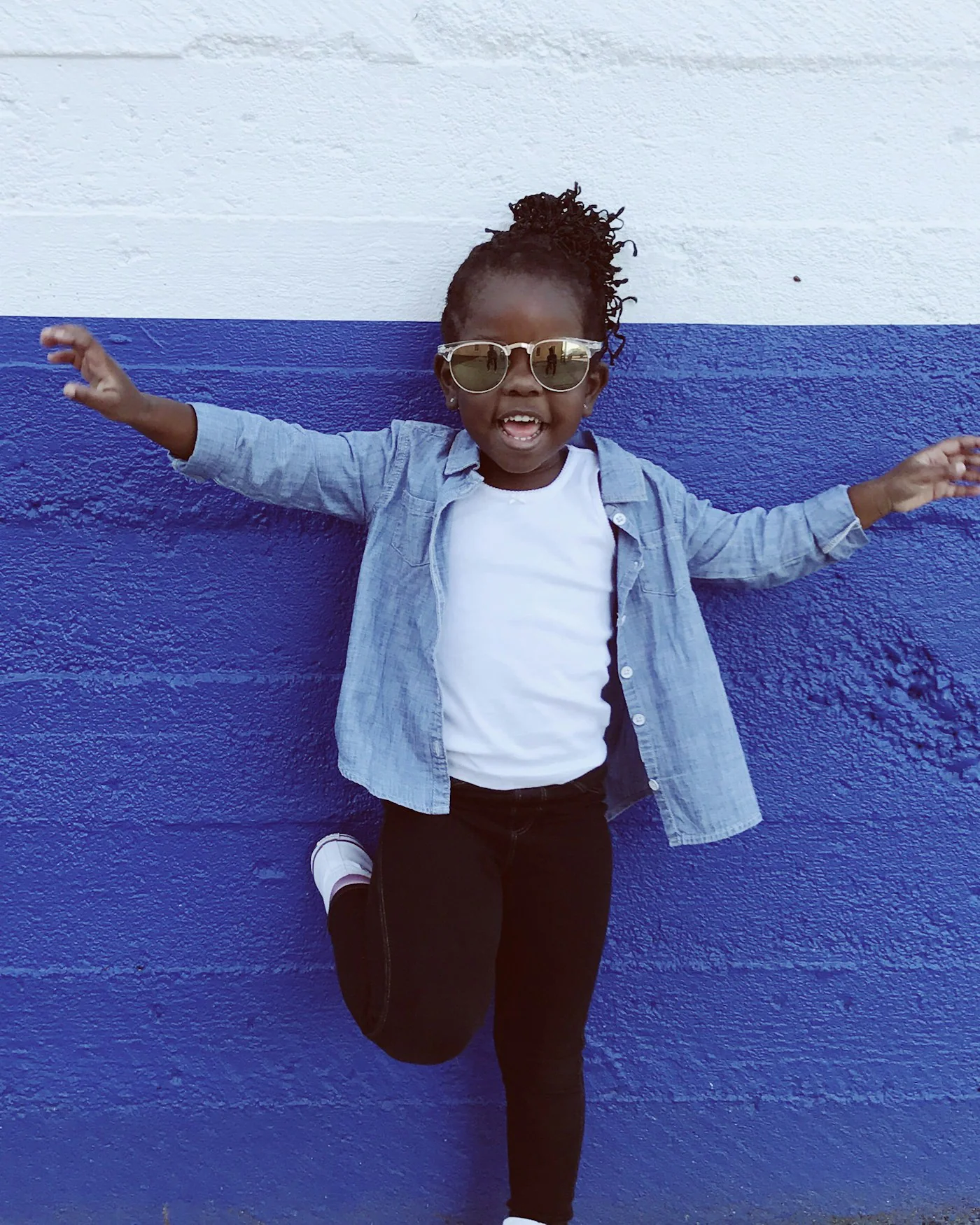 Girl in a light denim jacket jumping against a blue wall — detail