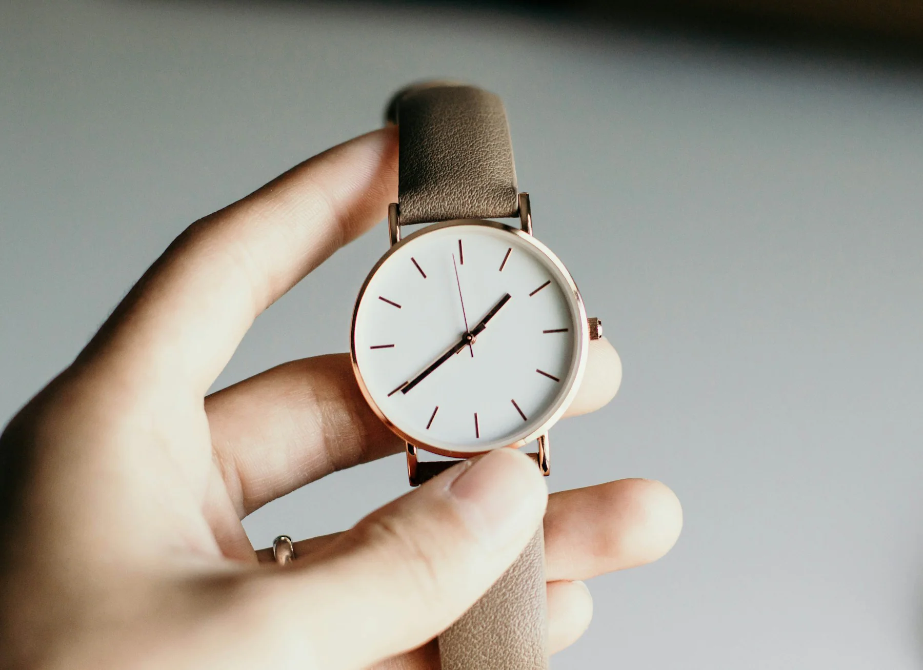 Hand holding a minimalist watch with a white dial and tan strap